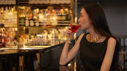 Sitting beautiful drinking alone in Cosmopolitan red cocktail waiting friends or couple at bokeh lighting luxurious beverage counter nightclub at pub and restaurant on Friday meeting night. Vinosity.
