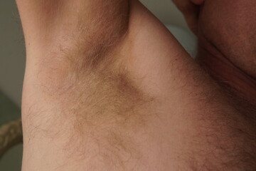 Raised Arm with Visible Armpit Hair. A close-up of a man's raised arm, clearly showing his light-colored armpit hair. The focus is on the armpit area, capturing the natural texture and color of the ha