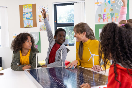 Female teacher engaging with diverse students on solar energy project in classroom, at school