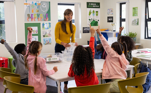 In school, female teacher engaging diverse students in recycling lesson, raising hands