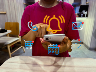Notification Alert and Digital Communication Concept. Young entrepreneur checks smart phone with floating notification icons for messages, calls, emails calendar events real-time communication at cafe