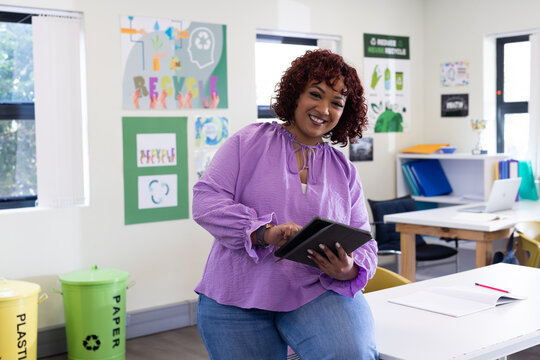 Smiling female teacher using tablet in classroom, promoting recycling and sustainability, at school