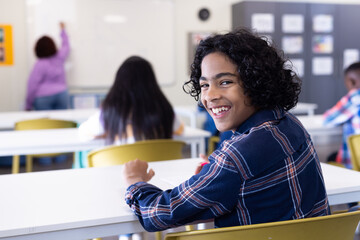 Smiling boy in classroom turning around, engaging with lesson on whiteboard, at school
