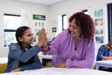 Female teacher and girl high-fiving in classroom, celebrating success and teamwork, at school