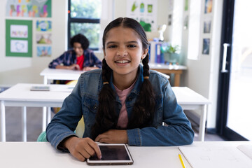 Smiling girl using tablet in classroom, enjoying learning at school