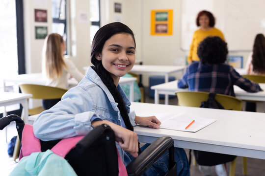 Smiling girl in wheelchair attending school class, engaging with female teacher