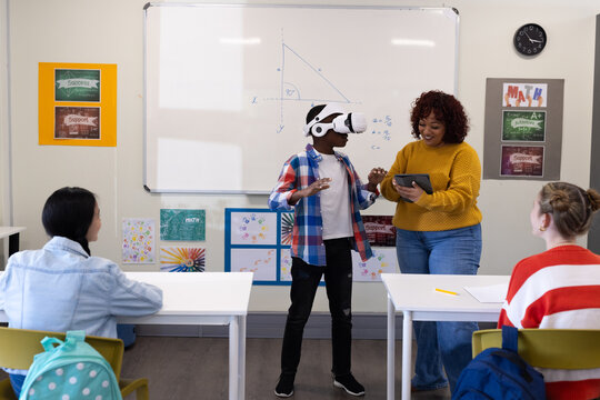 Female teacher guiding african american boy using vr headset in classroom, at school