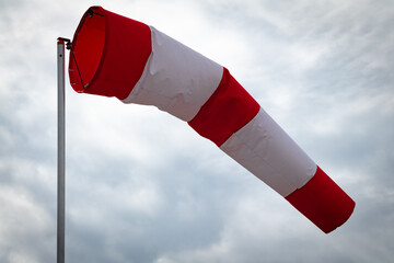 A windsock on a metal pole against a cloudy sky indicates a wind blowing from the left at about 3-6...