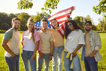 Portrait of happy smiling young people friends in casual clothes holding USA flag standing together...