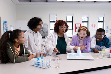 Diverse students in science class watching chemistry experiment with female teacher, at school