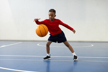 Young boy dribbling basketball on indoor court, focused and determined