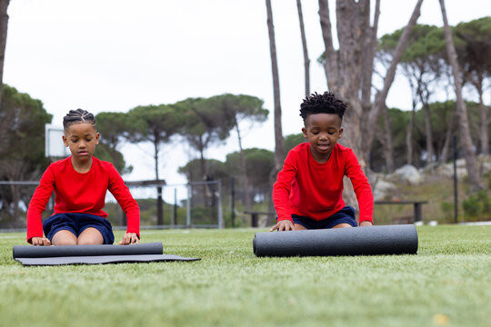 Diverse boys rolling yoga mats on grass, preparing for outdoor exercise session