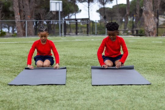 Diverse boys rolling yoga mats on grass, preparing for outdoor school activity - Powered by Adobe
