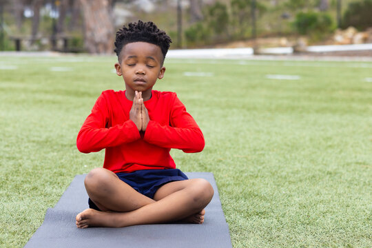 African american boy practicing yoga on mat outdoors, meditating with eyes closed, copy space