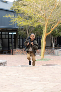 Young boy running with backpack outside school, looking determined and focused