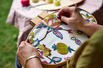 Over-the-shoulder close-up view of a woman embroidering a pattern on fabric held in an embroidery...