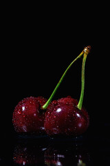 wet two cherries on black background close up