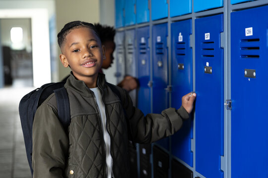Opening locker in school hallway, boy smiling and wearing backpack