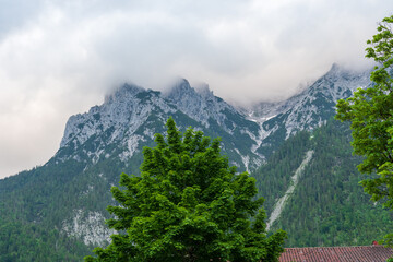 Zugspitze rises majestically through a veil of drifting clouds, its rugged, snow-dusted peaks cutting through the moody sky—Germany’s highest mountain cloaked in dramatic alpine mystery.