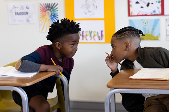 In school, two diverse boys whispering and sharing secrets during classroom activity