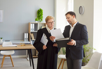 Judge woman in professional outfit black robe and man standing reviewing judiciary documents in...