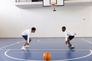 Diverse boys playing basketball in gym, practicing dribbling and defense skills