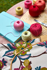 Close-up of a small garden table with embroidery supplies on a warm summer day. Colorful threads,...