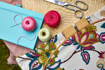 Close-up of a small garden table with embroidery supplies on a warm summer day. Colorful threads,...