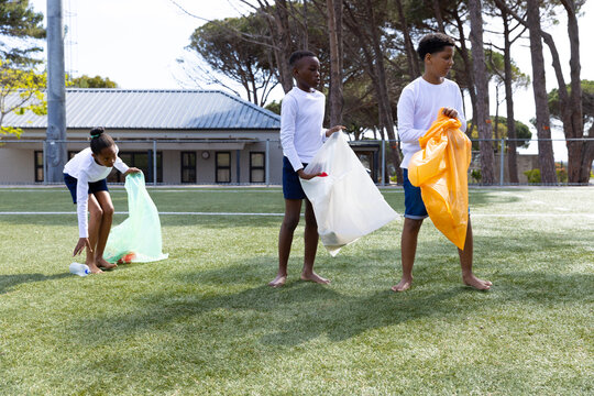 Cleaning school field, diverse students collecting trash in colorful bags, teamwork outdoors