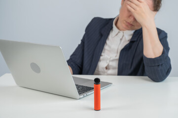 Caucasian businesswoman working on laptop. Disposable vape in foreground. 