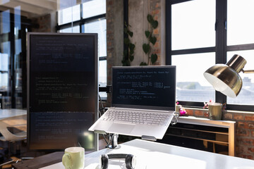 Laptop and monitor displaying code in modern office with natural light
