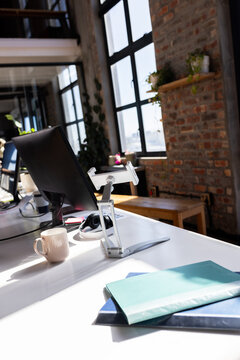 Modern office desk with computer monitor, coffee mug, and folders by window