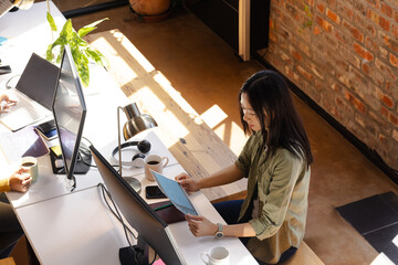 Asian woman coding on tablet at modern office desk with coffee
