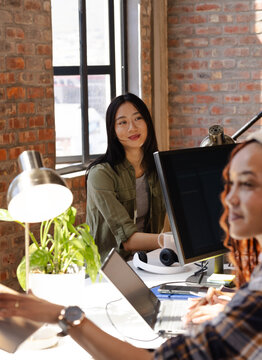 Asian woman collaborating with colleague at office desk, coding on computer