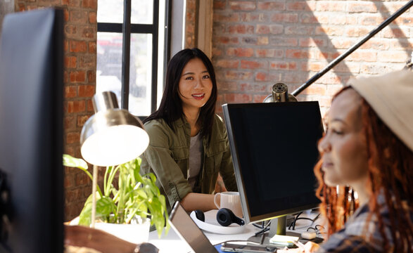 Diverse women collaborating on coding project at modern office, smiling and focused