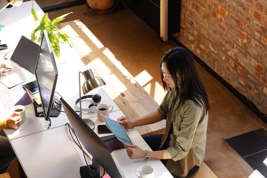 Asian woman coding on tablet at modern office desk with coffee