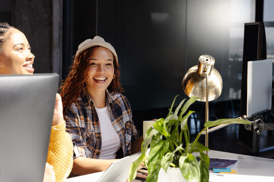 Diverse women collaborating on coding project at modern office, smiling and engaged