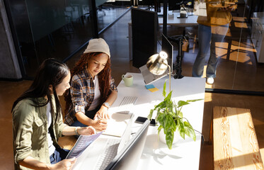 Diverse women collaborating on coding project at modern office desk with laptops