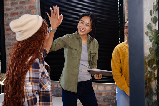 Celebrating successful project completion, Asian woman high-fiving colleague in office