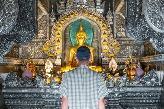 Man tourist standing inside ornate Silver Temple with golden buddha statue, intricate carvings and shimmering surfaces in Chiang Mai, Thailand. Rear view. Wat Sri Suphan Buddhist temple