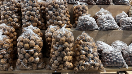 Shelled walnuts are neatly arranged on a counter in transparent bags. In the background, bags filled with hazelnuts and other nuts can also be seen.