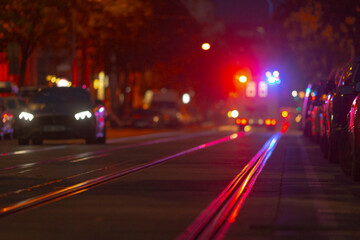 An urban street scene at night showcases the bright illumination of police lights, an array of moving vehicles, and gleaming streetcar tracks that enhance the nighttime atmosphere