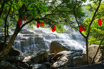 Red lanterns hanging over the Pongour Waterfall, cascading gently through forested rocks in Vietnam