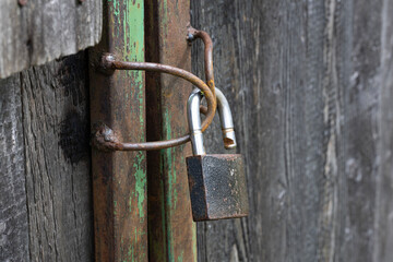 A close-up of a rusty padlock secured to a weathered wooden door with a chain. The door has a...