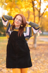 Portrait of a young beautiful red-haired girl in an autumn city park.