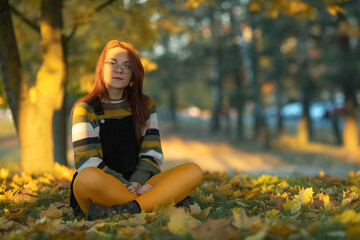 Portrait of a young beautiful red-haired girl in an autumn city park.
