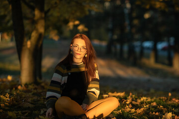 Portrait of a young beautiful red-haired girl in an autumn city park.