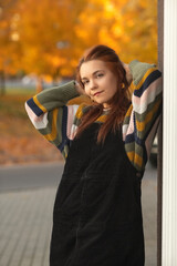 Portrait of a young beautiful red-haired girl in an autumn city park.