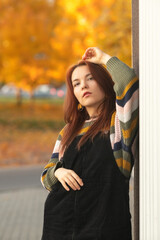Portrait of a young beautiful red-haired girl in an autumn city park.