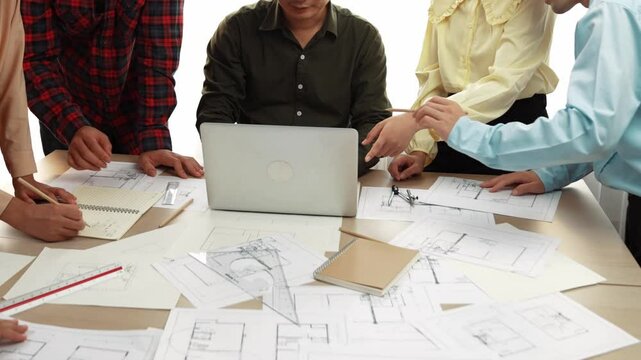 Architect and safety engineer discussion about building blueprint displaying on laptop on table with architectural document and wooden block scatter around at modern office. Closeup. Delineation.
